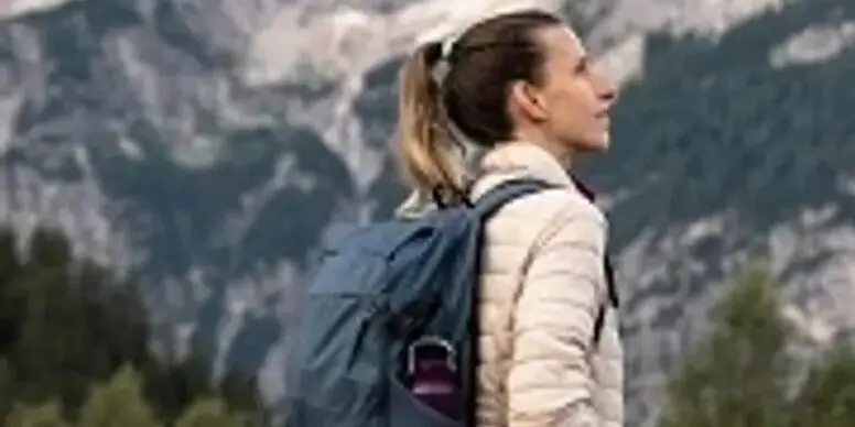 A woman with a backpack is standing in front of some mountains.