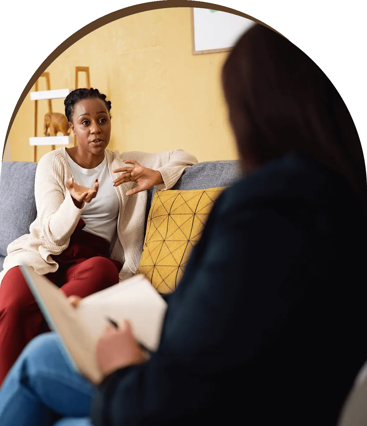 Group-1321317394.png A woman sitting on top of a couch talking to another person.