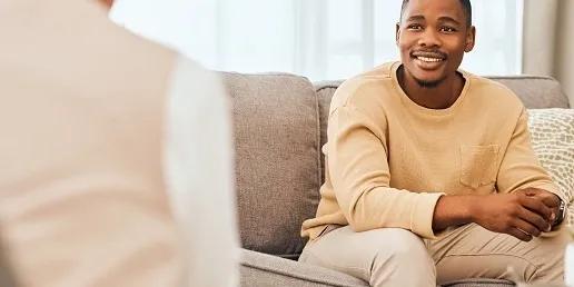 rs=w_516,h_258,cg_true A man sitting on top of a couch next to another person.