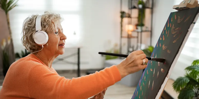 rs=w_776,h_388,cg_true A woman is painting on canvas in an orange shirt.